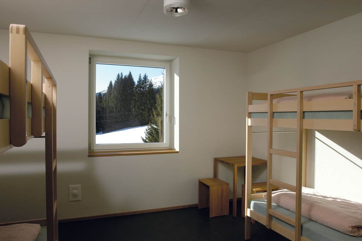 Una habitación con literas, una mesita pequeña y una ventana con vistas a árboles y nieve.