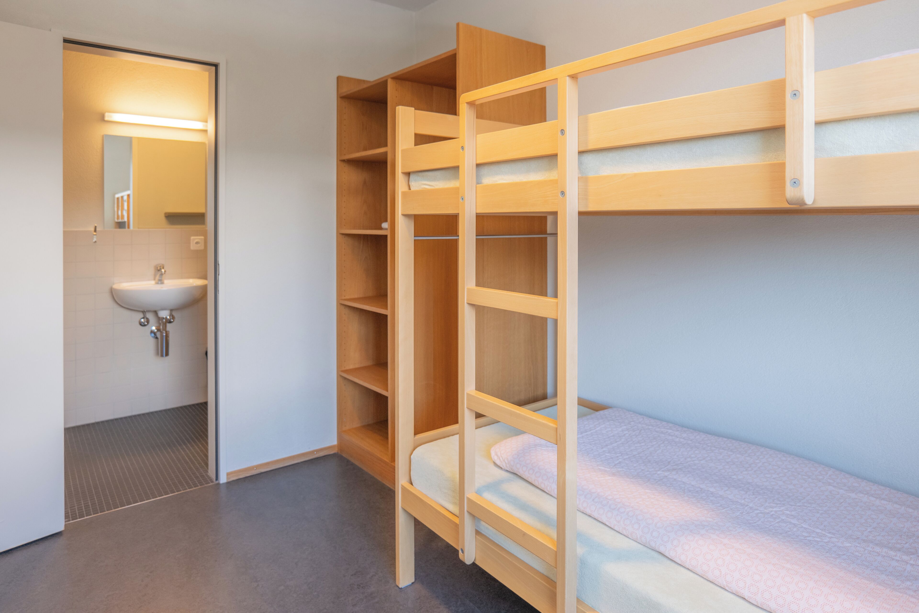 A bunk bed room with a wooden bunk bed, a single bed, and a built-in shelf unit.