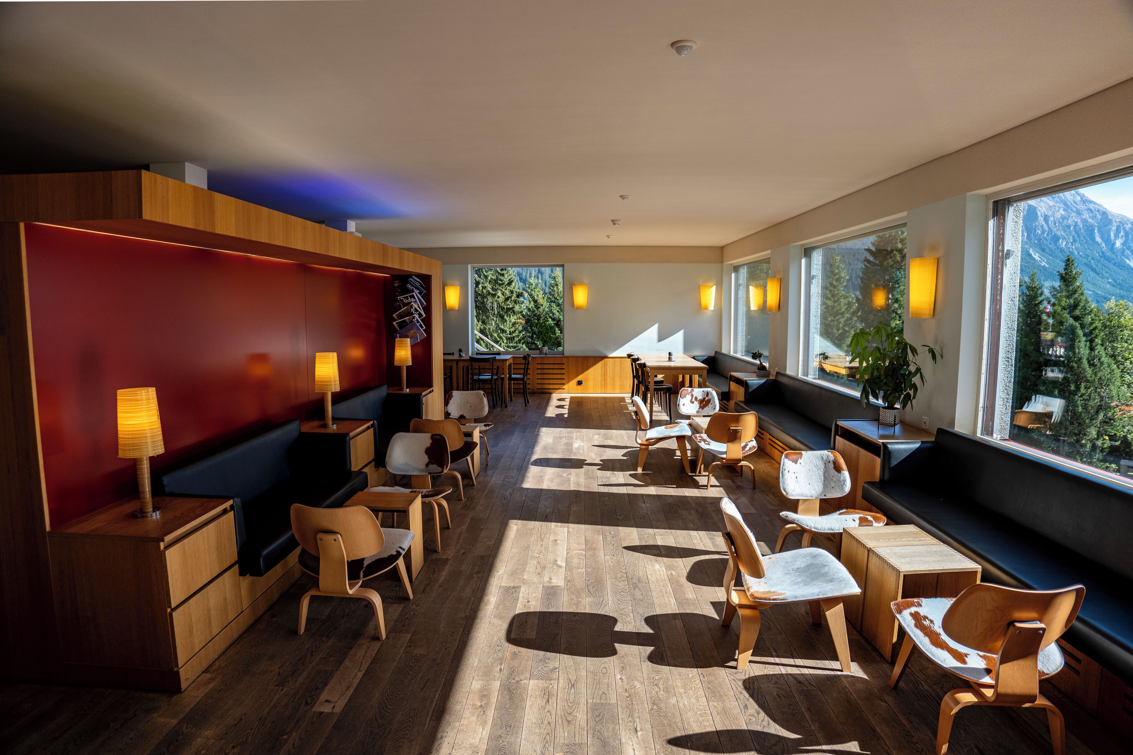Un moderno vestíbulo de hotel con muebles de madera, una pared de acento roja y grandes ventanales con vistas a la montaña.