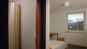 Une chambre à coucher avec un lit, une fenêtre donnant sur la montagne, une table de chevet en bois et un rideau de douche.