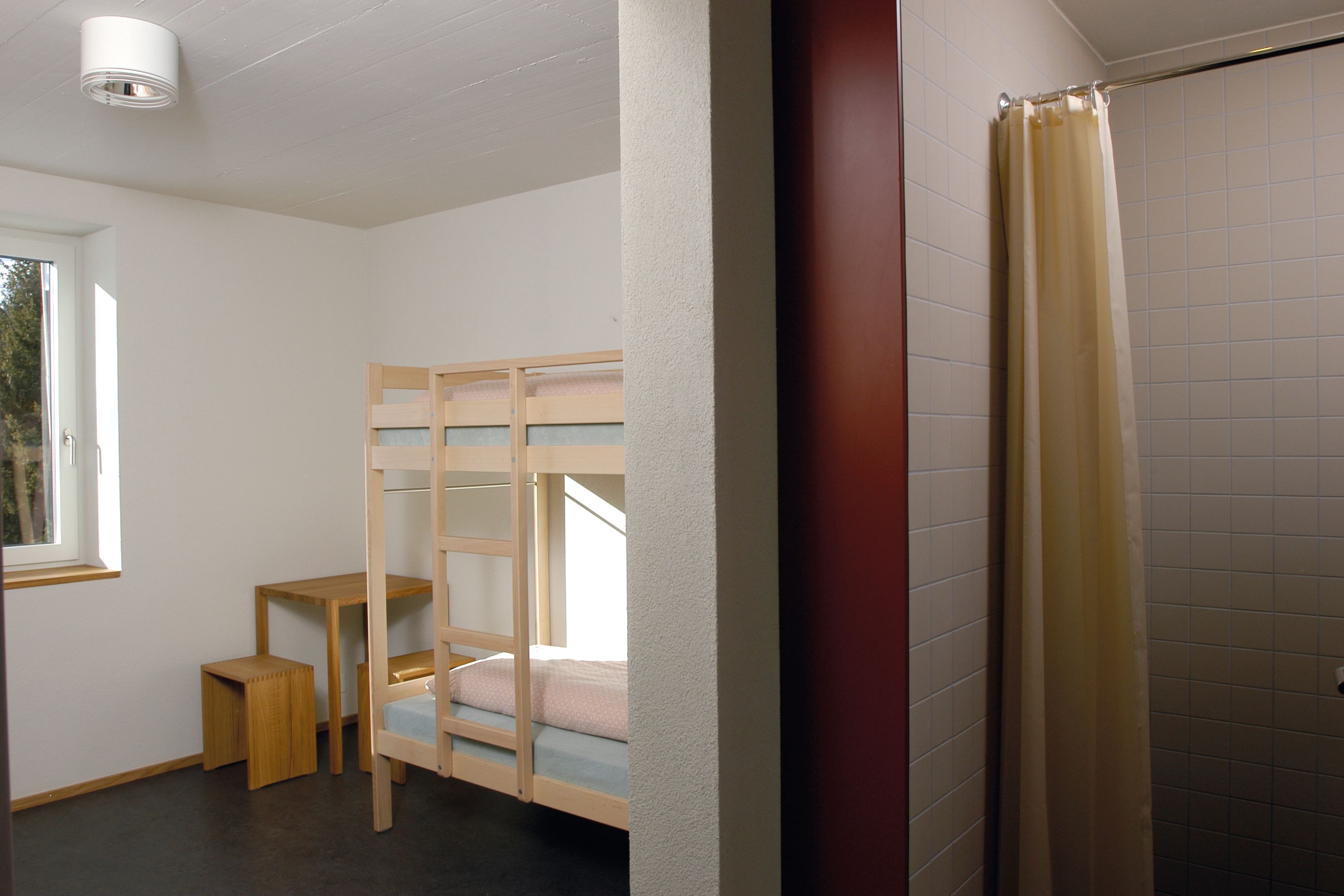 Ein Zimmer mit einem Etagenbett, einem kleinen Holztisch und einem Fenster.