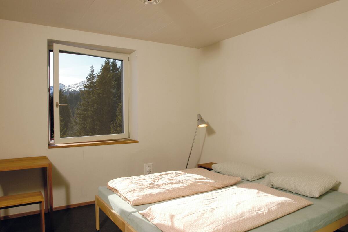 Un dormitorio con una cama individual, una mesita de noche, una lámpara y una ventana con vista a la montaña.