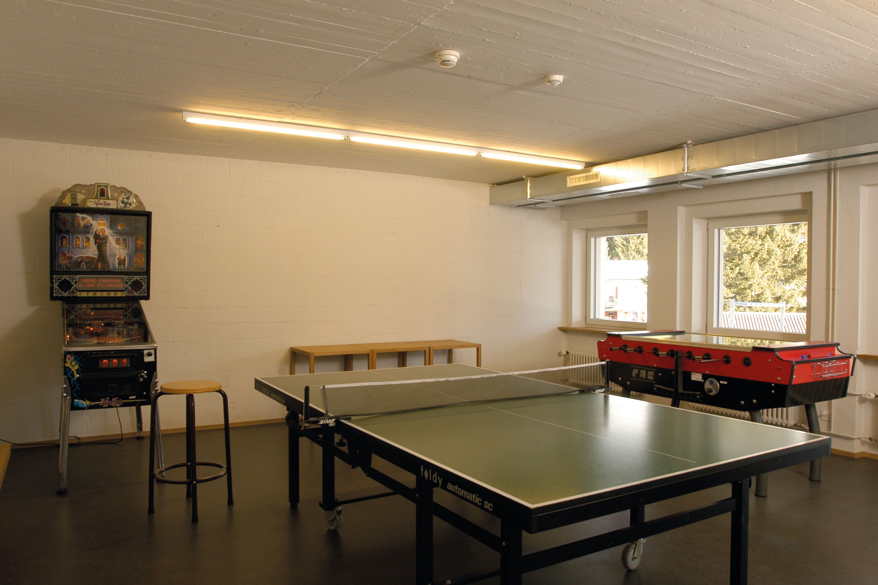 Una habitación con mesa de ping pong, mesa de futbolín y jukebox.