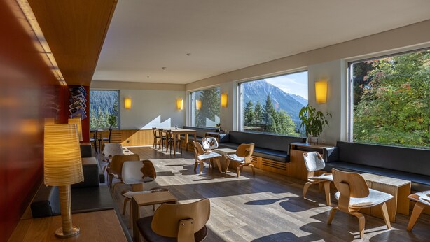Un comedor moderno con muebles de madera, ventanas amplias y vistas a montañas.