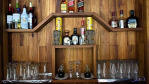 A wooden bar with shelves holding various liquor bottles and glasses. - Hotel Alkamar (Cóbano)