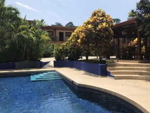 Una piscina con borde de azulejos, rodeada de palmeras y un edificio con tejado de cerámica.