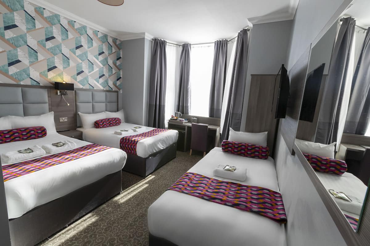 Habitación de hotel con dos camas, un escritorio, una silla, un televisor y una ventana con cortinas.