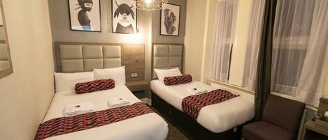 A hotel room with two beds, a chair, and artwork on the wall.