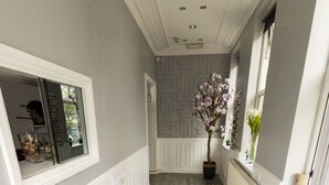 Un couloir d’hôtel avec un paillasson bleu sur lequel on peut lire « EURO HOTEL HAMMERMITH », des lambris blancs, un plancher en bois et une plante en pot ornée de fleurs.