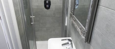 A modern bathroom with a glass-enclosed shower, a white sink, and a large mirror.