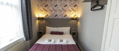A neatly made bed with a patterned bedspread, two bedside lamps, and a wall-mounted shelf with a hanger.