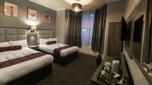 Une chambre d’hôtel avec deux lits, un téléviseur à écran plat, une table de chevet avec une lampe et des œuvres d’art accrochées au mur.
