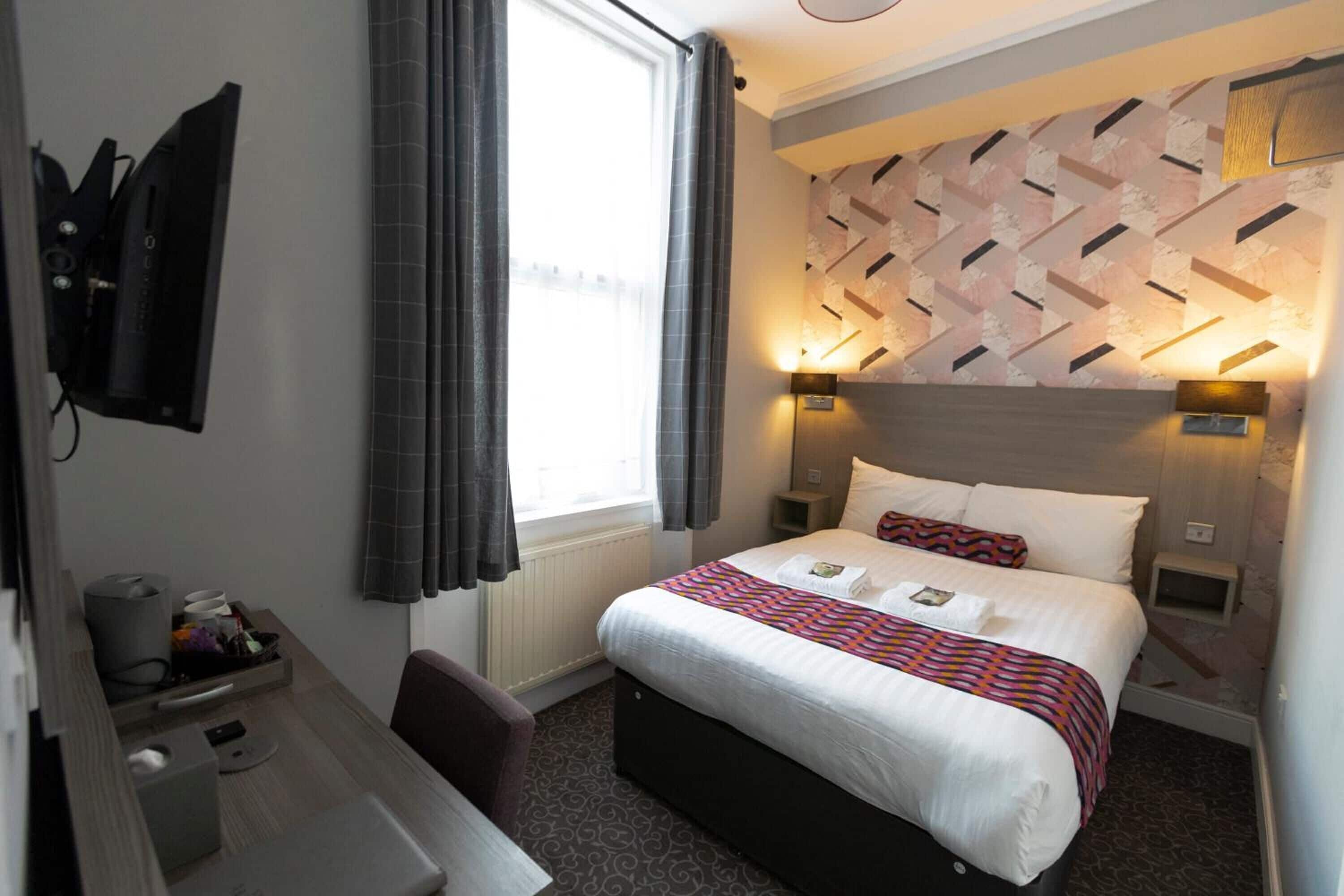 Ein Hotelzimmer mit Bett, Nachttischen, Schreibtisch, Stuhl, Fernseher und einem Fenster mit Vorhängen.