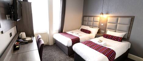 A hotel room with two beds, a desk, and a television.