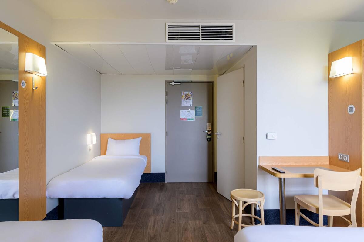 A hotel room with two beds, a desk, a chair, and a small table.