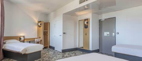 A hotel room with two beds, a desk, a chair, and a wardrobe.