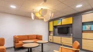 A modern lounge area with orange seating, round tables, and a flat-screen TV on a wooden cabinet. - B&B HOTEL Marseille Les ports (Marseille)