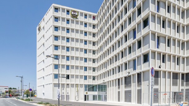 A modern building with a grid-like facade, multiple windows, and a prominent sign on the top. - B&B HOTEL Marseille Les ports (Marseille)