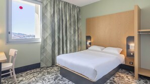 A hotel room with a bed, a chair, a window with a view, and a curtain. - B&B HOTEL Marseille Les ports (Marseille)