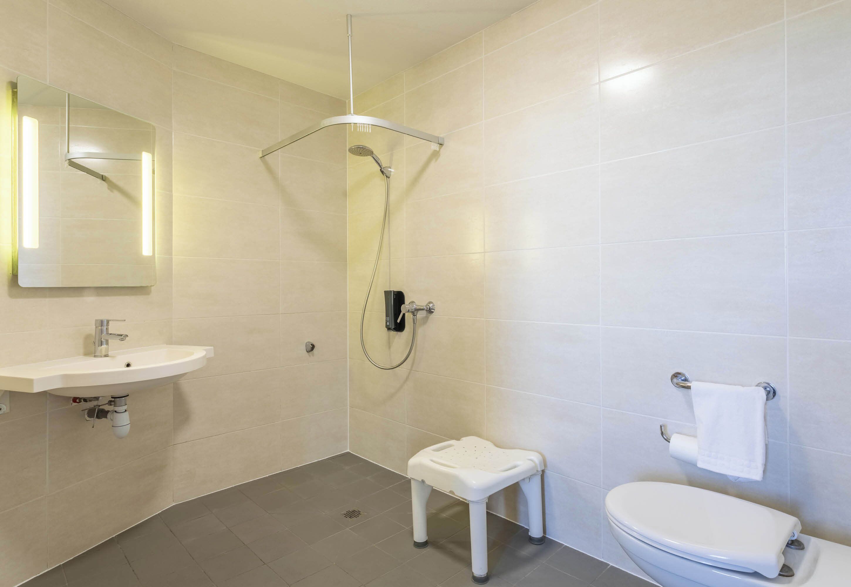 Un baño moderno con ducha, inodoro, lavamanos y un pequeño taburete.