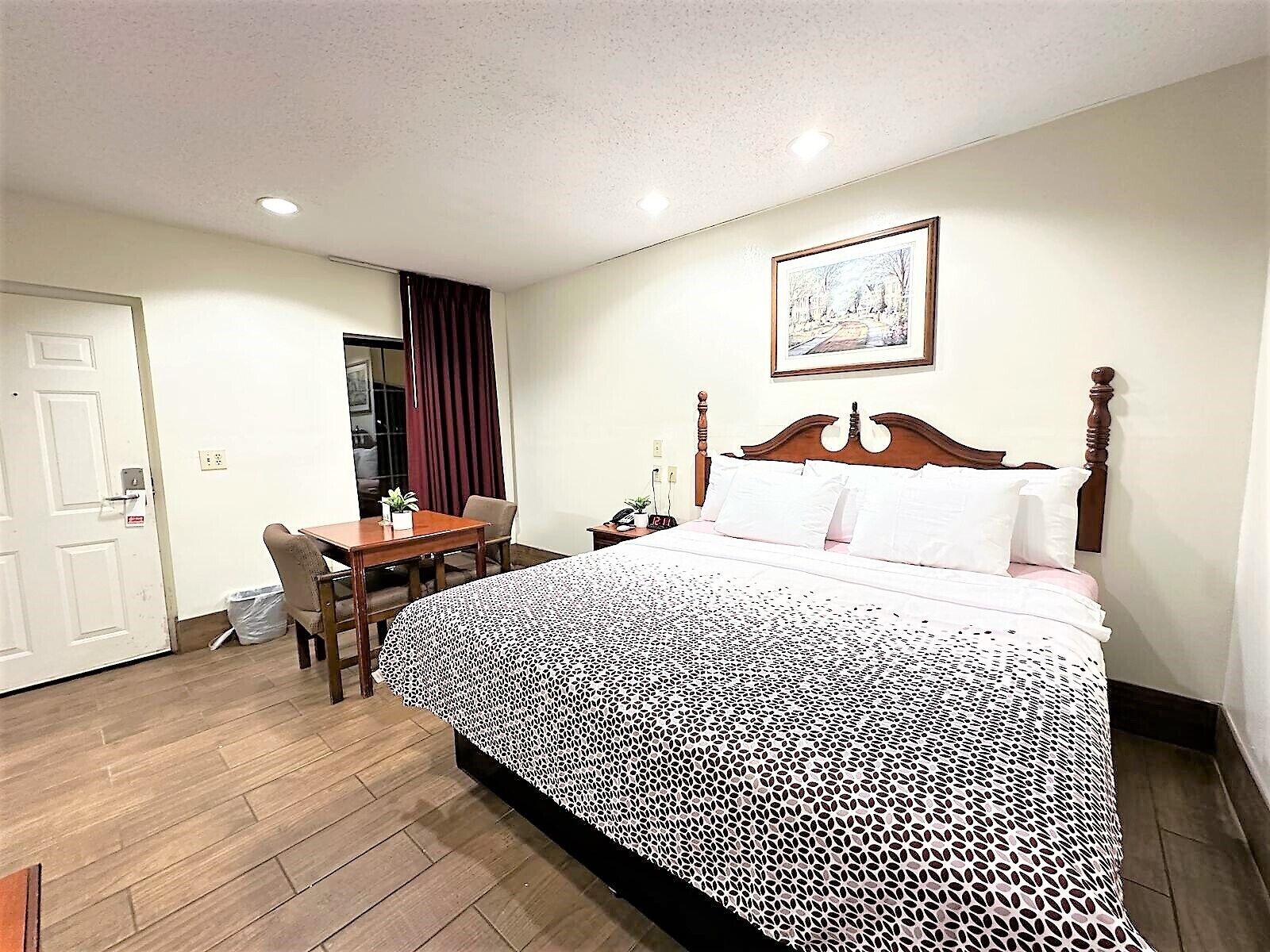 Habitación de hotel con cama, escritorio, silla, mesita de noche y un cuadro en la pared.