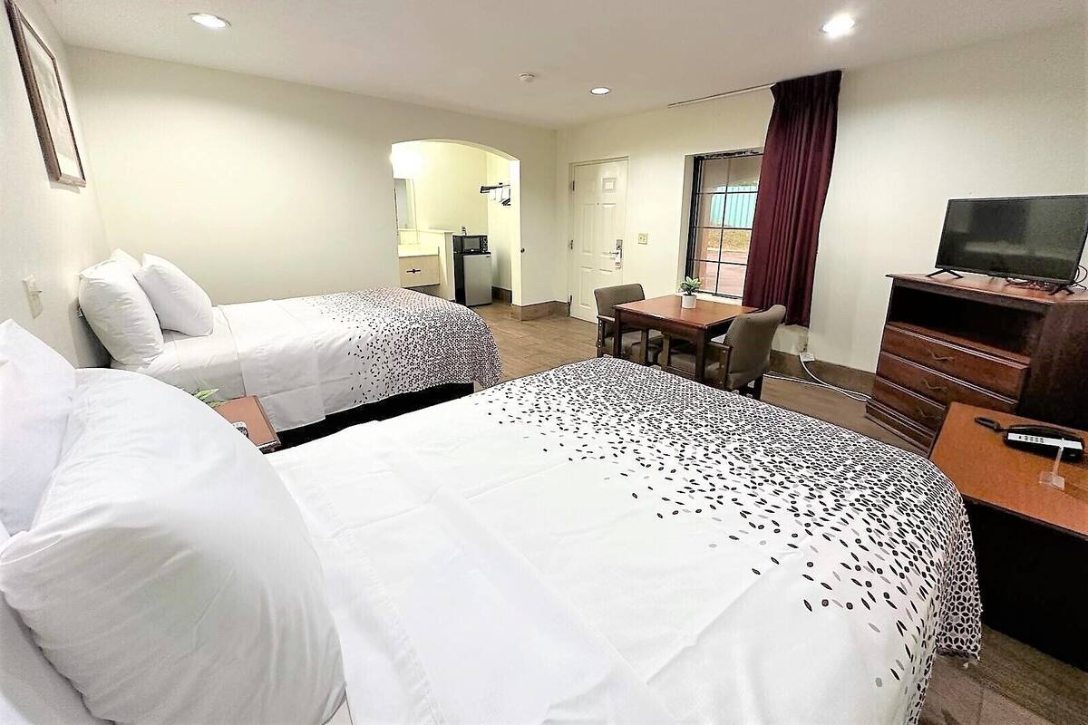 A hotel room with two beds, a desk, a television, and a bathroom visible in the background.