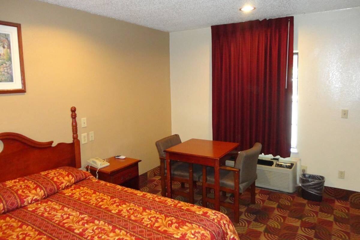 A hotel room with a bed, a desk, a chair, a telephone, and a window with curtains.
