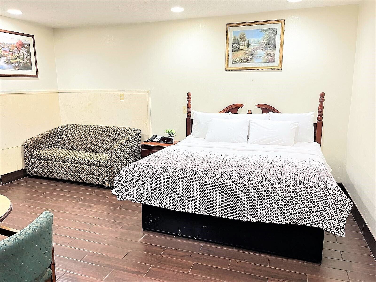 Habitación de hotel con una cama, una silla, una mesita y un cuadro en la pared.