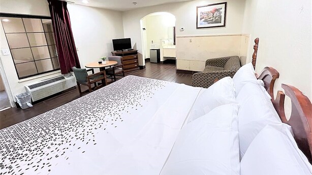 A hotel room with a bed, a desk, a chair, a TV, and a window with curtains. - Budget Inn (Northport)