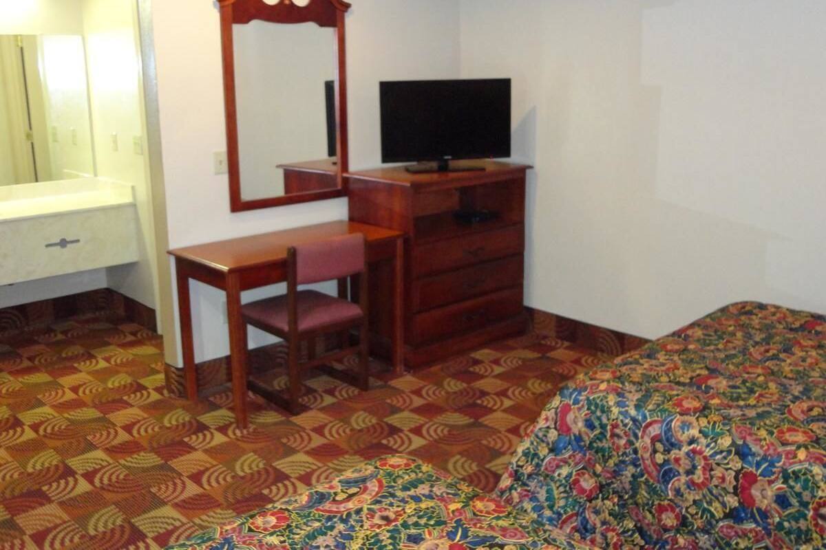 A bedroom with a bed, a dresser, a chair, a mirror, and a television.