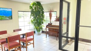 A dining area with a piano, a large potted plant, and a fire extinguisher. - Budget Inn (Northport)