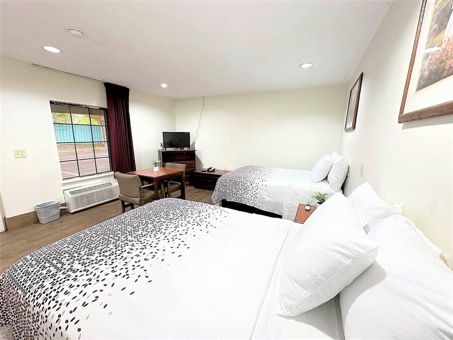 Una habitación de hotel con dos camas, un escritorio con silla, televisor y ventana con cortinas.