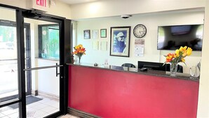 A reception area with a red counter, framed certificates, a clock, and a TV. - Budget Inn (Northport)