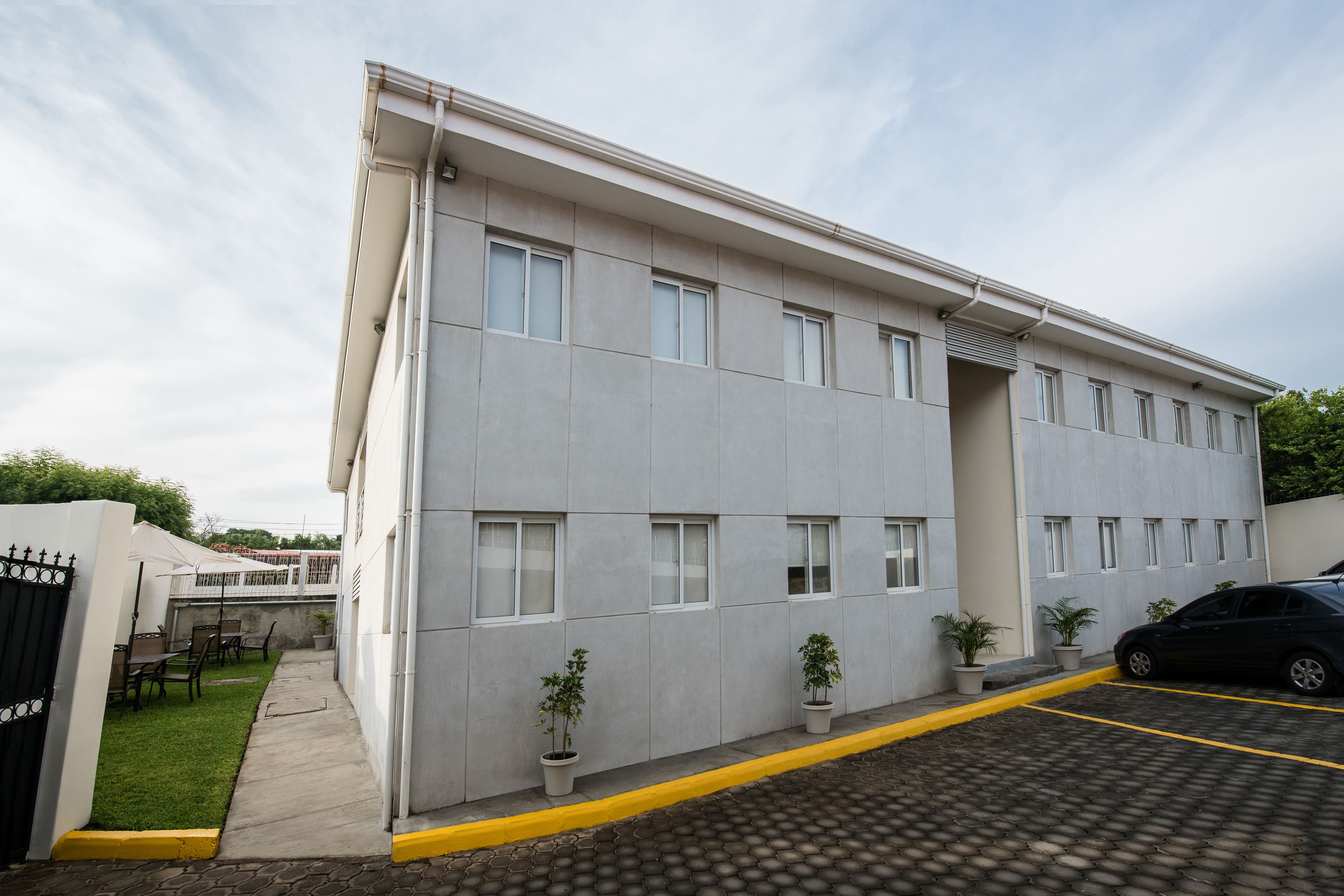 A modern building with a flat facade, multiple windows, and a parking area with yellow lines.