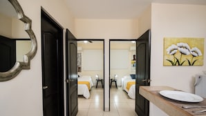 Quarto de hotel com duas camas, banheiro com espelho e pia, e um quadro na parede.