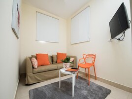 Una sala de estar con un sofá beige, cojines naranja, una mesita blanca con una planta y un sillón naranja.
