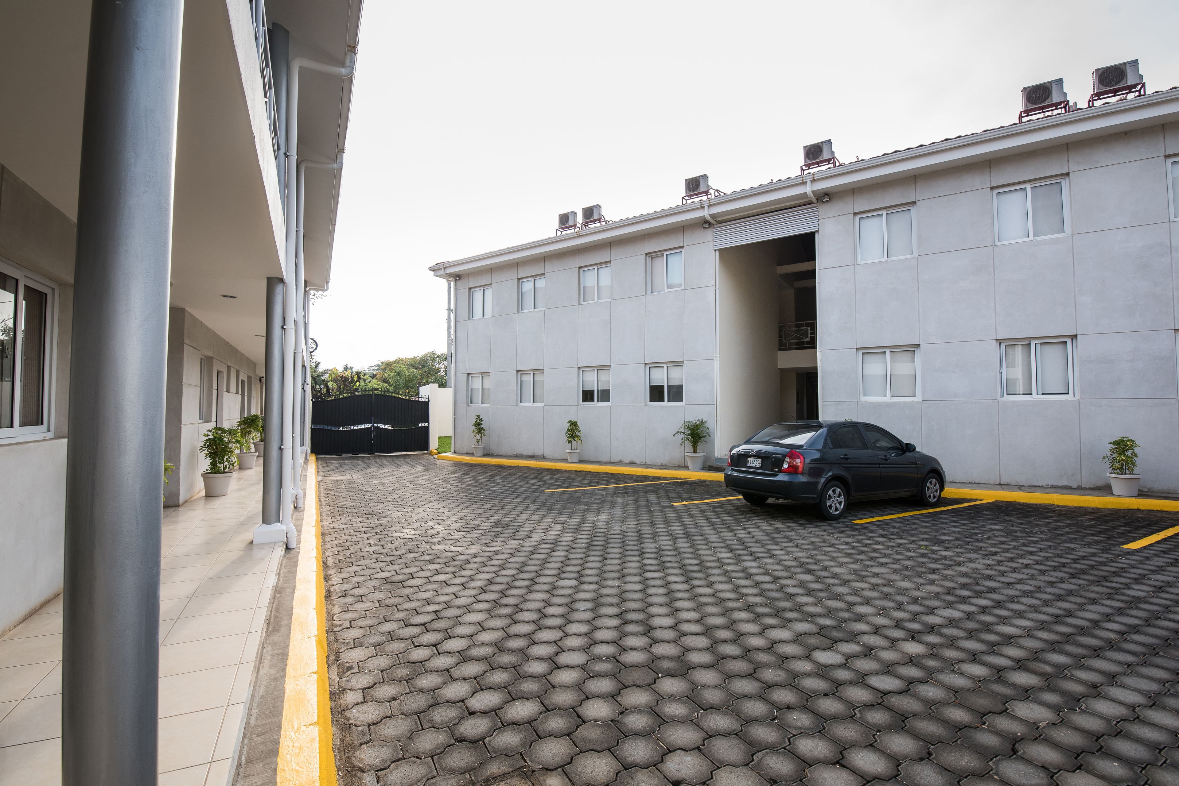 A parking area with a paved surface, a car, and a building with multiple windows and air conditioning units.