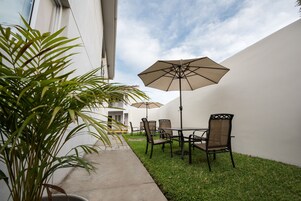 Un patio al aire libre con una mesa, sillas, un paraguas grande y una planta en maceta.