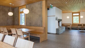 Een ruime eetruimte met houten tafels en stoelen, een betonnen toonbank en hanglampen.