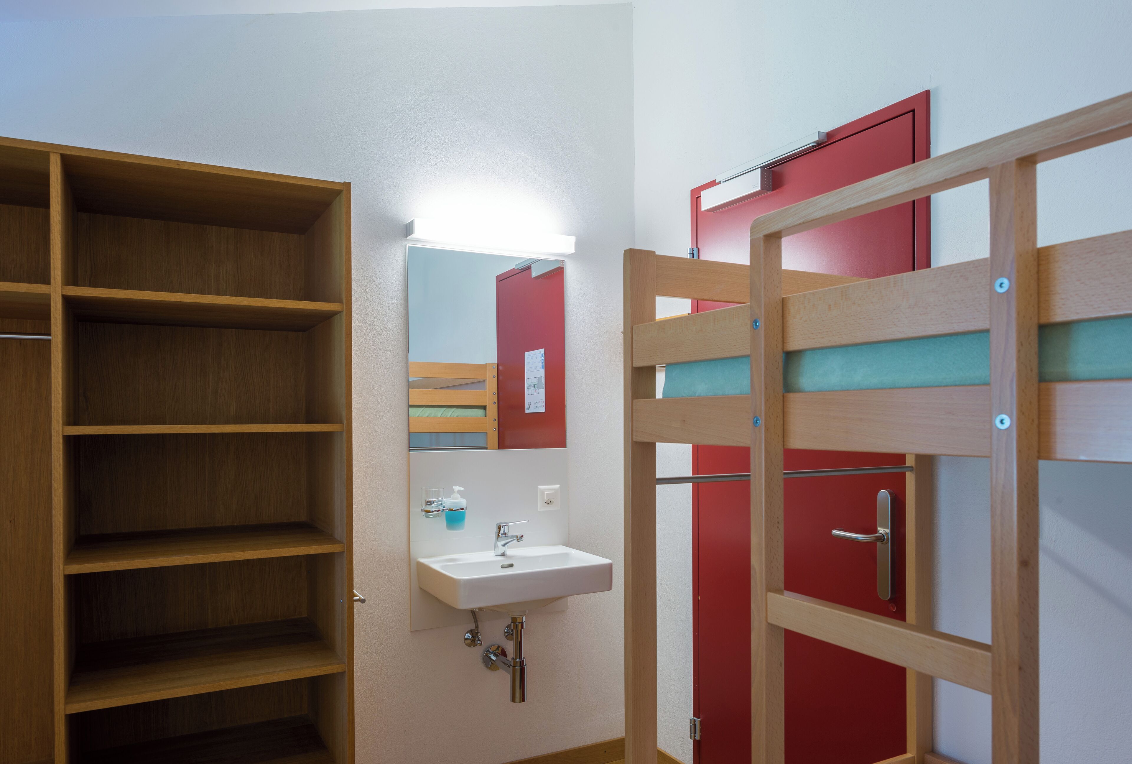 A bathroom with a wooden shelf unit, a white sink, and a red door.