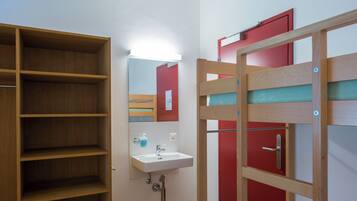A bathroom with a wooden shelf unit, a white sink, and a red door.
