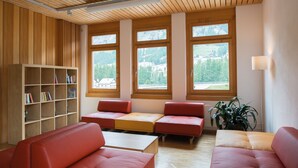 Een modern interieur met houten lambrisering, grote ramen, rode zitplaatsen en een boekenkast.