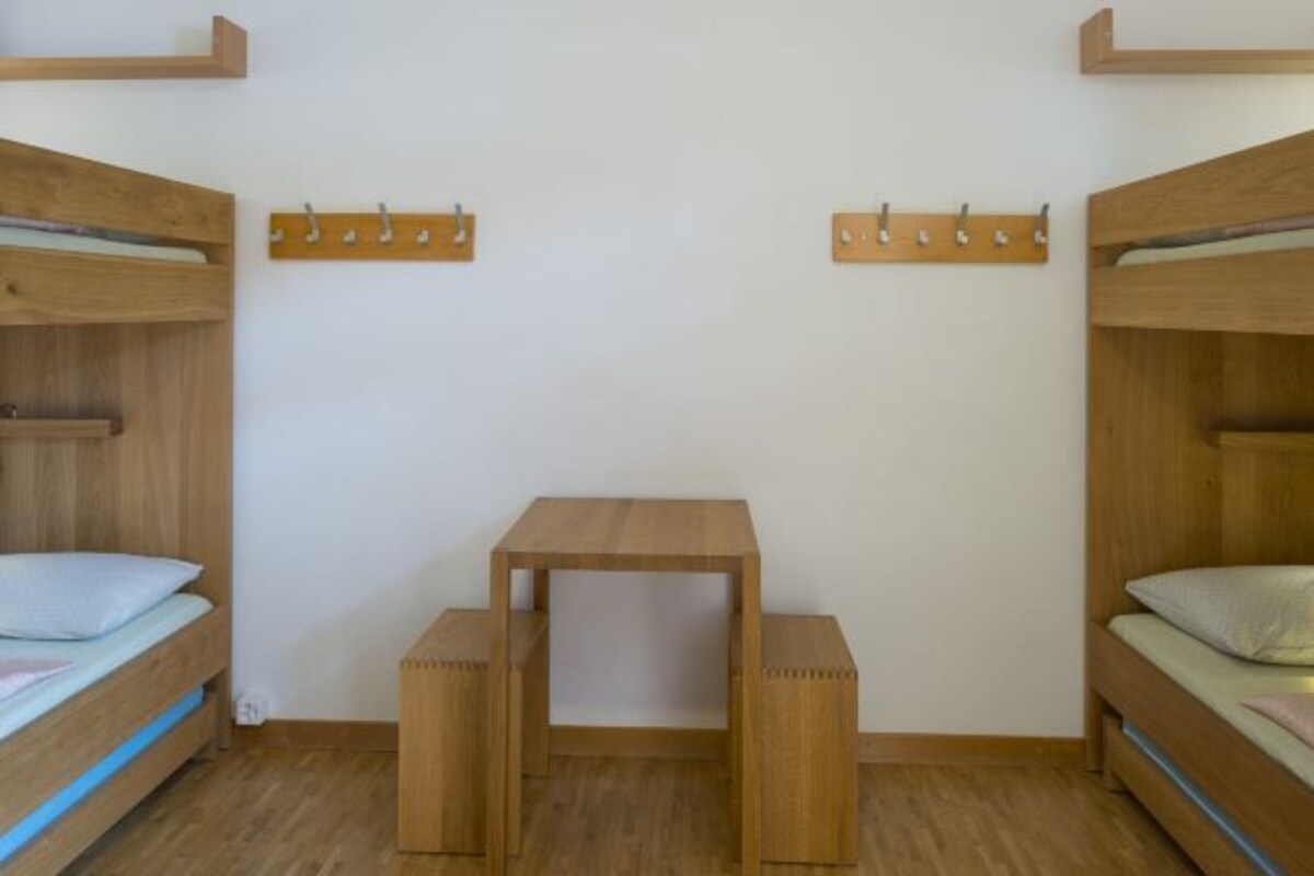 Une pièce avec deux lits superposés, une petite table en bois et deux crochets pour manteaux fixés au mur.
