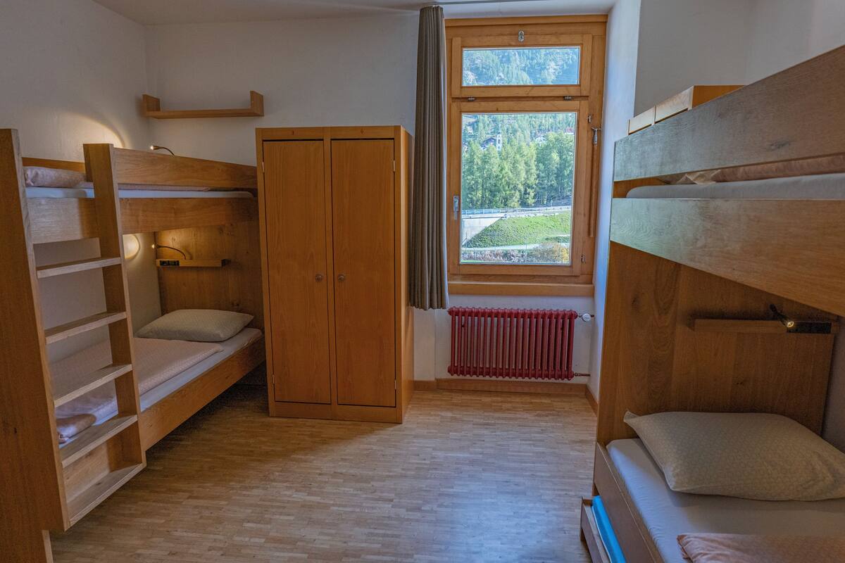 Une chambre avec des lits superposés, une armoire et une fenêtre donnant sur un paysage verdoyant.
