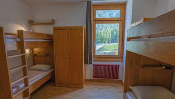 A room with bunk beds, a wardrobe, and a window with a view of greenery.
