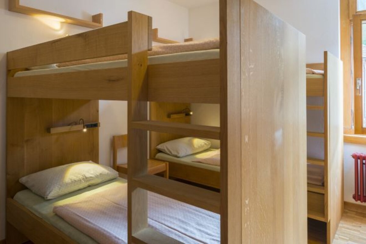 Une chambre avec un lit superposé en bois, une petite table de chevet et une lampe.