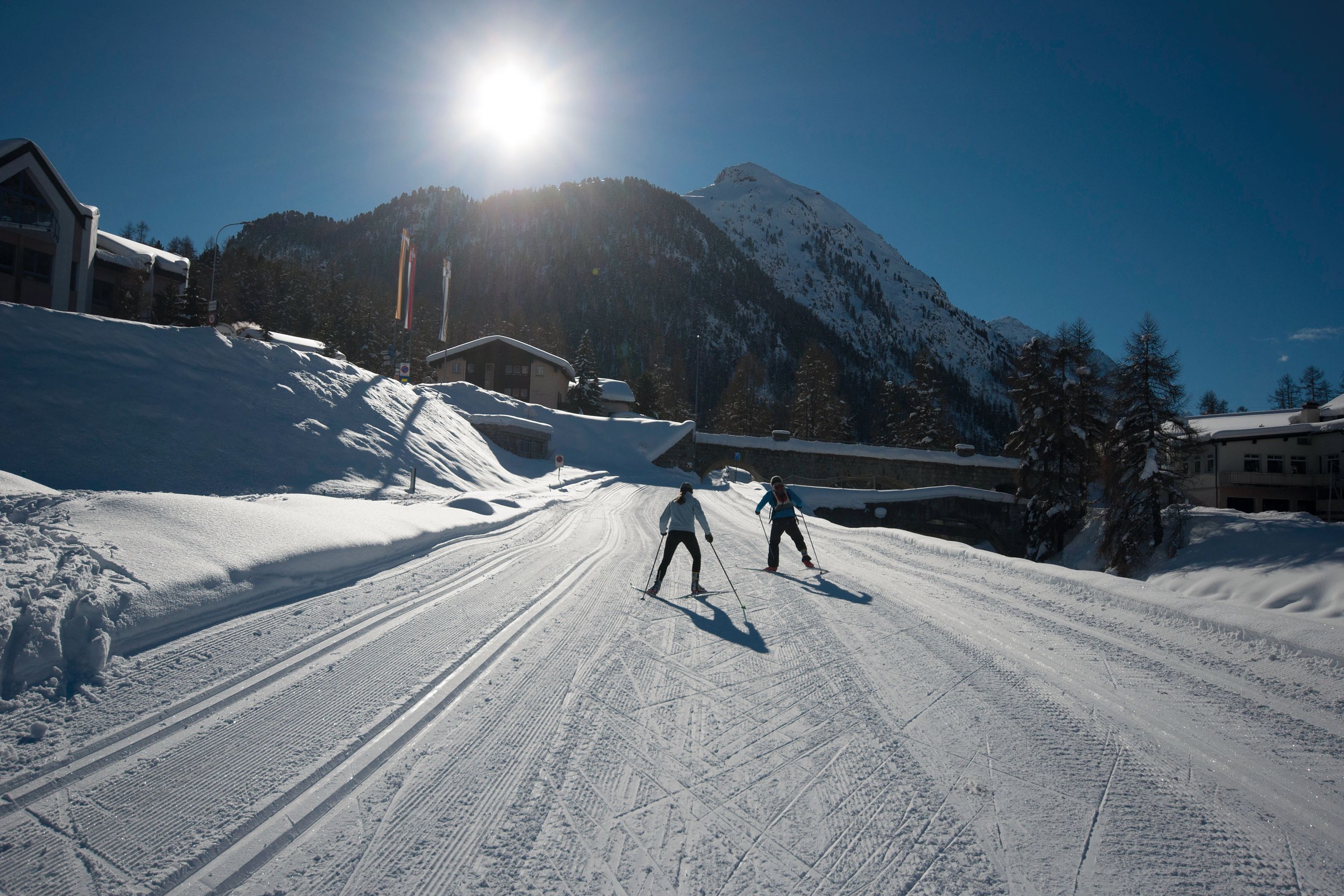 A ski slope with skiers, a mountain backdrop, and buildings in the distance.