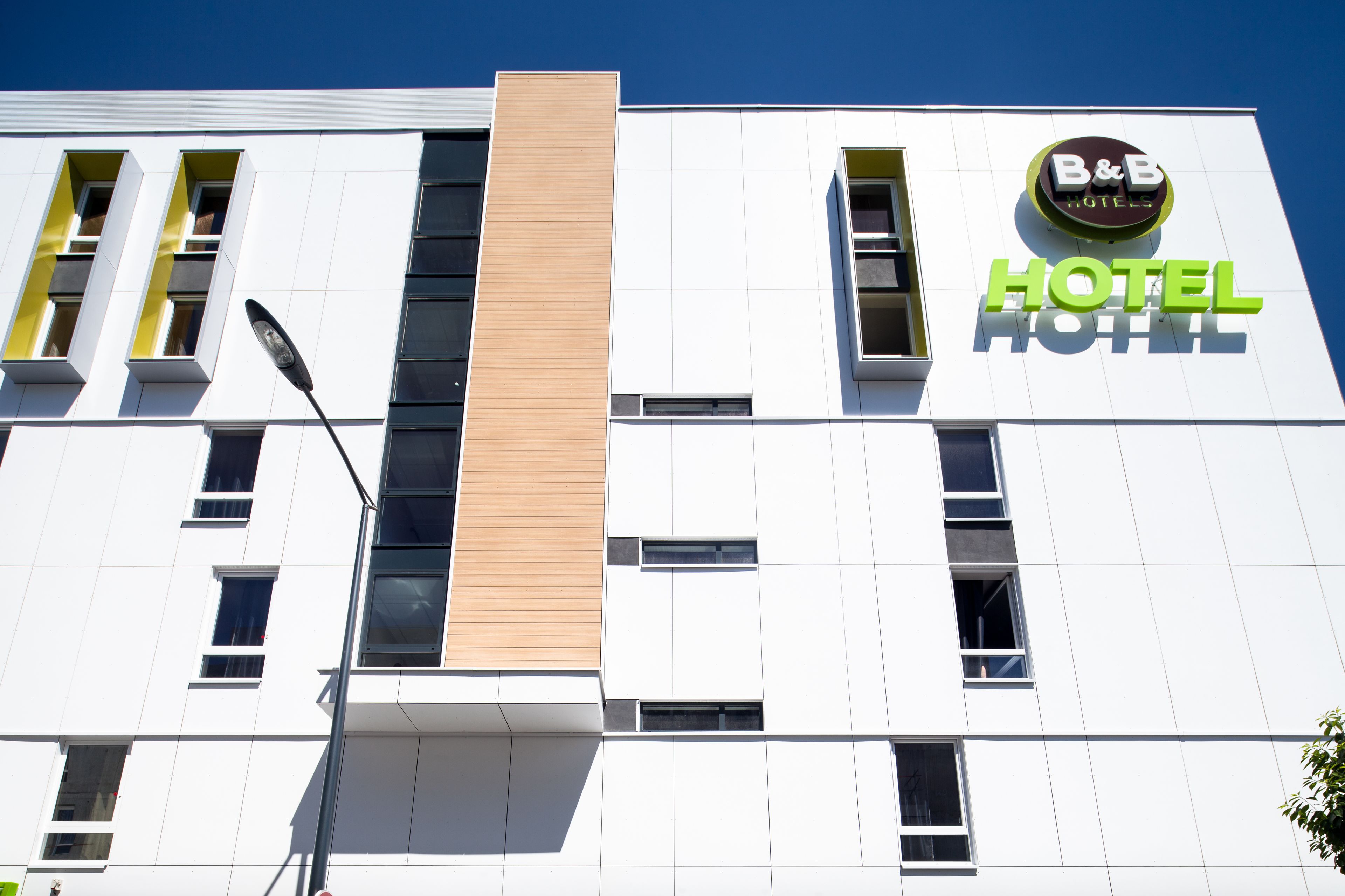 A modern hotel building with a prominent B&B Hotels sign, large windows, and a clean, white facade.