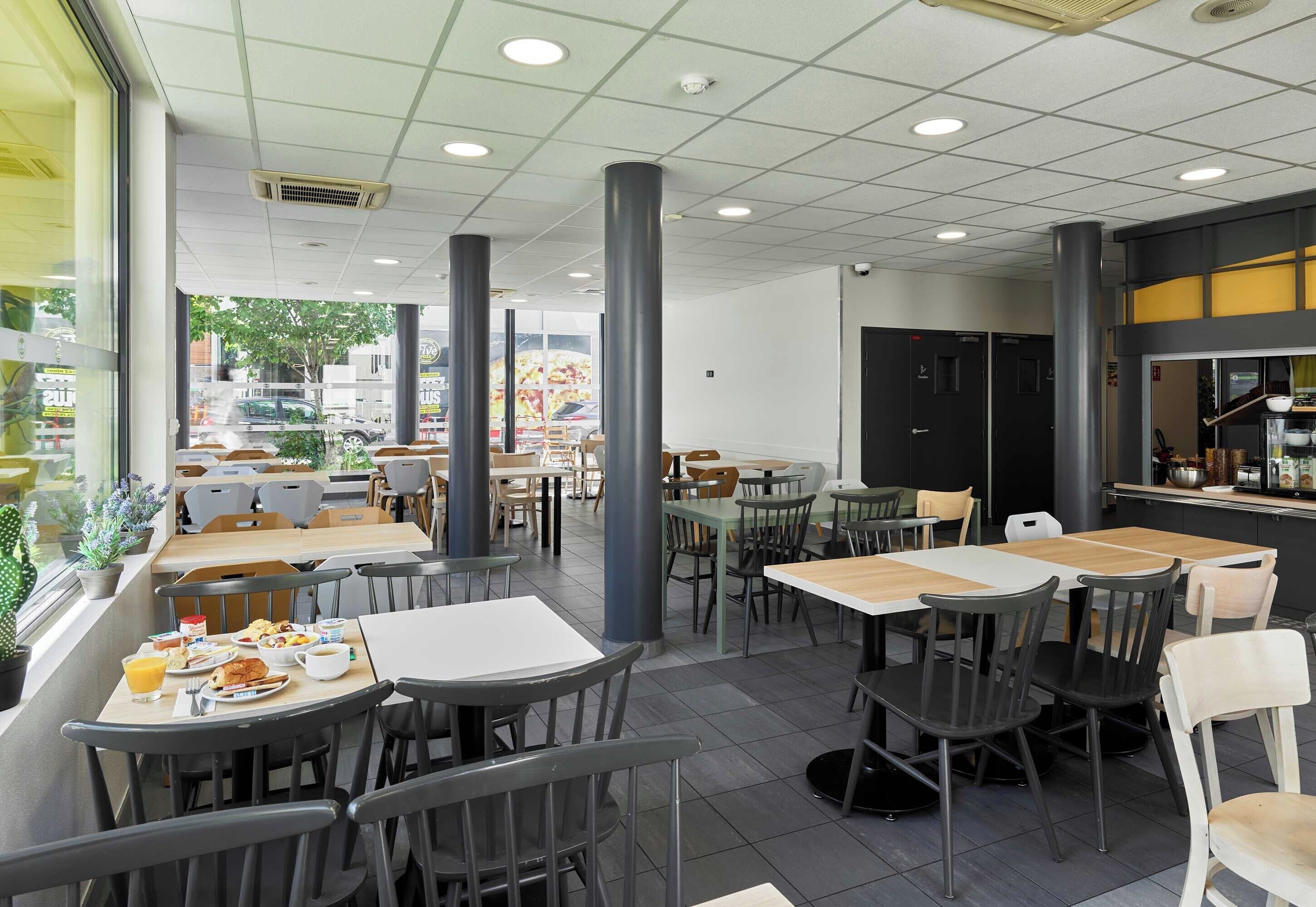 Um café espaçoso com várias mesas e cadeiras, grandes janelas e um design de interiores moderno.