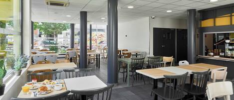 Um café espaçoso com várias mesas e cadeiras, grandes janelas e um design de interiores moderno.